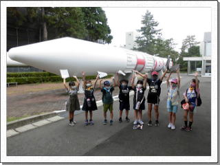 JAXAのロケットの前でバンザイする子ども達の写真